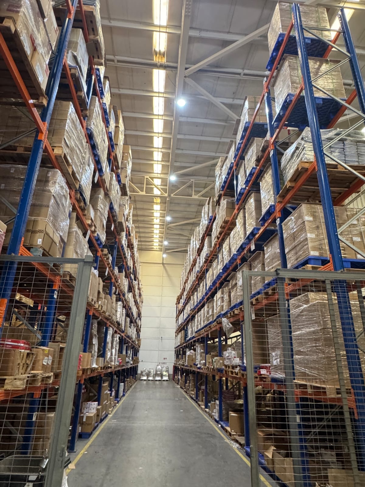 Pasillo de bodega industrial con racks altos, pallets y mercadería almacenada
